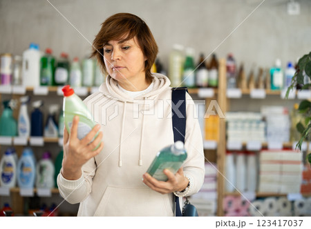 Woman buyer chooses shampoo or shower gel in household goods department of supermarket Woman buyer chooses shampoo or shower gel in household goods department of supermarket 123417037