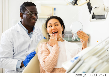 Dentist patient looks in the mirror at new tooth after surgery Dentist patient looks in the mirror at new tooth after surgery 123417571
