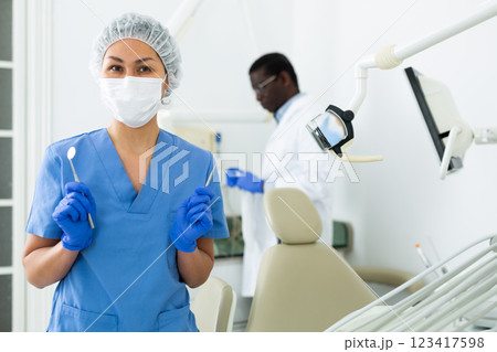 Female dentist standing in dental office with tools in hands 123417598