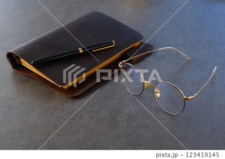 茶色の革のシステム手帳と金縁の眼鏡、ペンで、デスクワークをしているイメージ 茶色の革のシステム手帳と金縁の眼鏡、ペンで、デスクワークをしているイメージ 123419145