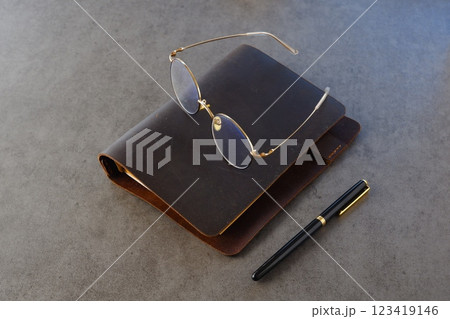茶色の革のシステム手帳と金縁の眼鏡、ペンで、デスクワークをしているイメージ 123419146