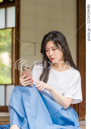 古民家の縁側で悩みながらスマホをタップする若い女性 古民家の縁側で悩みながらスマホをタップする若い女性 123419486