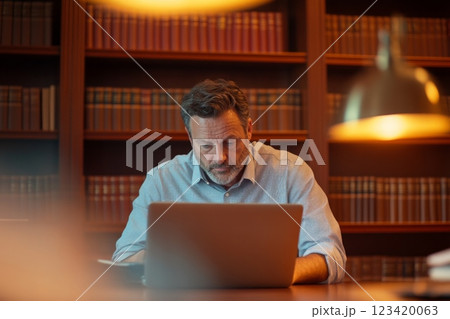 Lawyer working at desk with laptop and surrounded by legal books in office 123420063