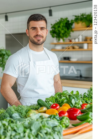 A joyful chef stands confidently in a bright kitchen surrounded by fresh vegetables and greens 123420138