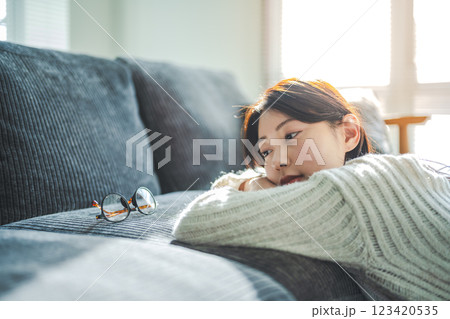 ソファに腕を置き、眼鏡を見つめる女性 ソファに腕を置き、眼鏡を見つめる女性 123420535
