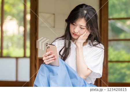 古民家の縁側でスマホを見ながら首を傾げる若い女性 123420815