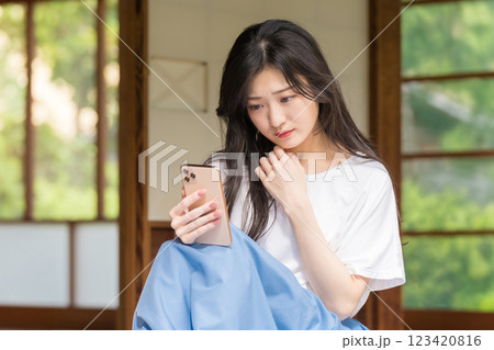 古民家の縁側でスマホを見ながら首を傾げる若い女性 123420816