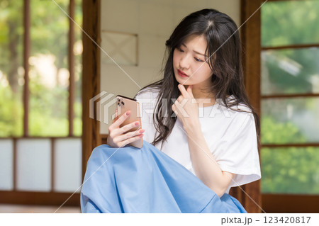 古民家の縁側でスマホを見ながら首を傾げる若い女性 123420817
