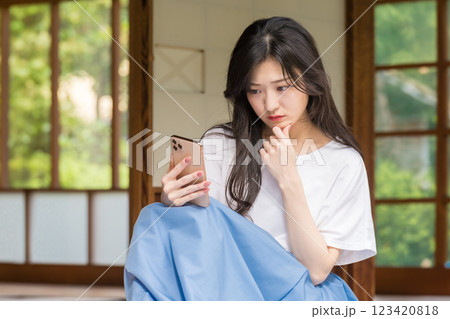 古民家の縁側でスマホを見ながら首を傾げる若い女性 123420818