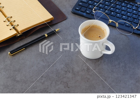 淹れたての美味しいコーヒーを飲みながら、ノートパソコンとシステム手帳でデスクワークをしているイメージ 123421347