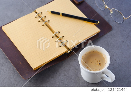 ミルクをたっぷり入れたコーヒー、カフェ・ラッテを飲みながら、システム手帳でデスクワーク中のイメージ 123421444