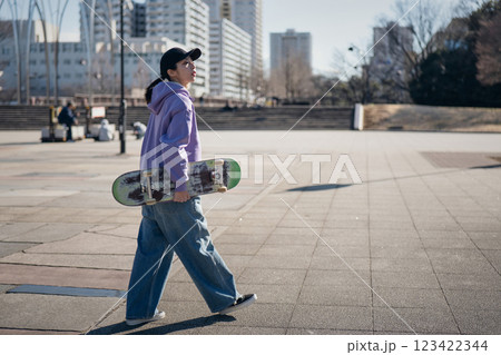 スケートボードを抱えて公園を歩くスケートボーダー 123422344