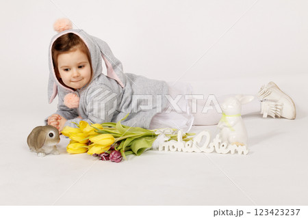 Cute Toddler in Bunny Costume Lying Next to Easter Decorations and Yellow Tulips 123423237