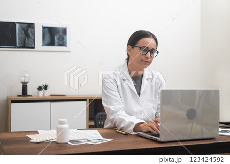 Digital Health Specialist: A female doctor, diligently working on her laptop, provides online medical assistance, conducts video conferences, and embodies the concept of telehealth.  123424592