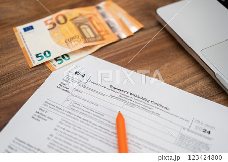 Employee filling out IRS form W-4 with euros and a laptop on a wooden desk. Payroll, tax withholding, and personal finance management concept Employee filling out IRS form W-4 with euros and a laptop on a wooden desk. Payroll, tax withholding, and personal finance management concept 123424800