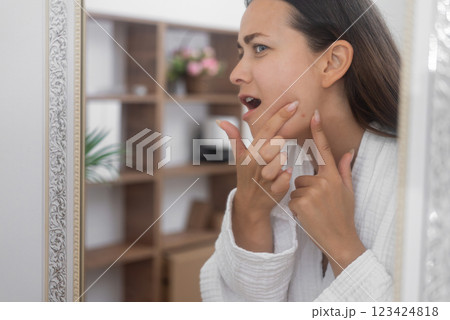 A distressed woman gazes into the bathroom mirror, feeling unhappy about her skin concerns.  123424818