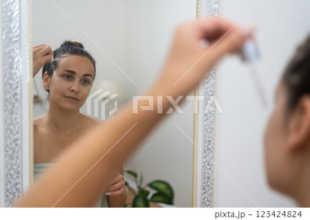 Mirror moment: A woman enhances her anti-aging skincare, using a serum dropper to apply hyaluronic acid in her home.  123424824