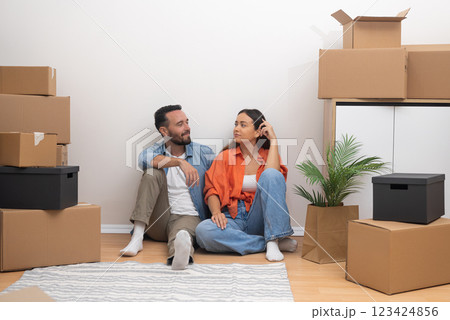 Happy newlyweds celebrate purchase of new apartment together sitting on floor among things collected in cardboard boxes after receiving keys from realtor 123424856