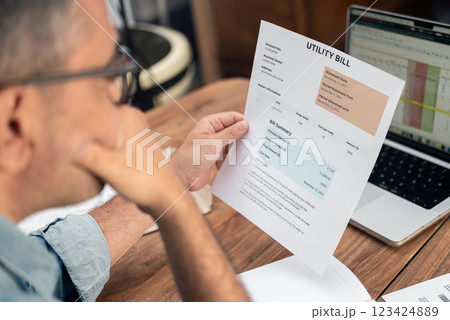 Grey haired male employee looks at utility bill attentively sitting at office workplace, thoughtful mature businessman studies household services expenses growth 123424889