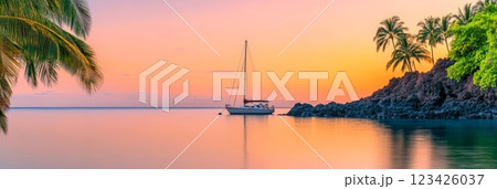 Sailboat rests peacefully in a calm bay as the sun sets, casting a warm glow over the water and silhouetting palm trees on a rocky outcrop, creating a serene tropical paradise scene 123426037