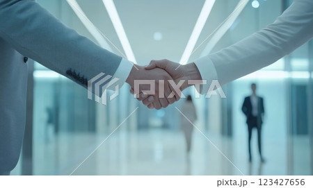 Two businessmen sealing a successful deal with a handshake in a modern office hallway, showcasing teamwork, trust, and negotiation skills in a corporate setting 123427656
