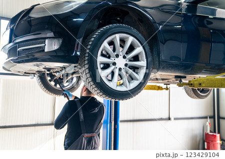 Serviceman checks car suspension on a column lift in car service Serviceman checks car suspension on a column lift in car service 123429104