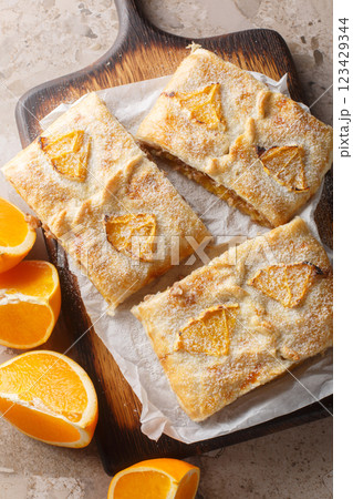 Orange strudel pie with jam, nuts, raisins and fresh fruits close-up on wooden board on table. Vertical top view Orange strudel pie with jam, nuts, raisins and fresh fruits close-up on wooden board on table. Vertical top view 123429344