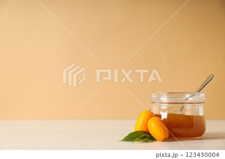 Kumquat and jar of jam on beige background, space for text 123430004