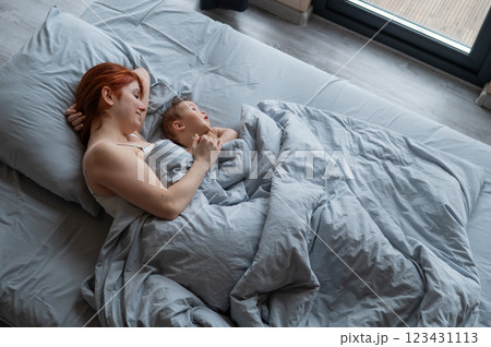 Top view of a red-haired Caucasian woman lying in bed with her baby son.  123431113