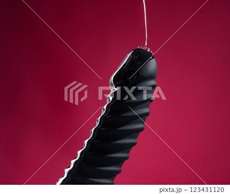 Lube pouring on black dildo on pink background.  123431120