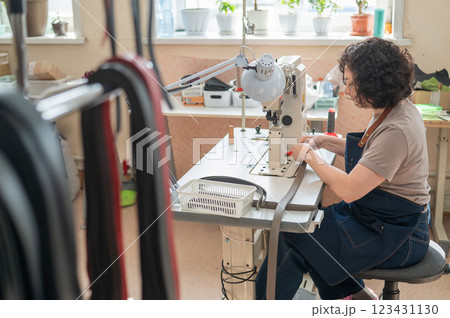 A woman tanner sews a leather belt on a sewing machine. A woman tanner sews a leather belt on a sewing machine. 123431130