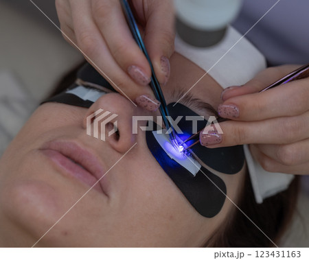 A woman undergoing eyelash extension procedure using an ultraviolet lamp. A woman undergoing eyelash extension procedure using an ultraviolet lamp. 123431163