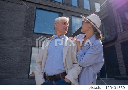 A woman in a hat and glasses hugs an elderly man in a white jacket from behind. Romantic relationships of mature people. A woman in a hat and glasses hugs an elderly man in a white jacket from behind. Romantic relationships of mature people. 123431280