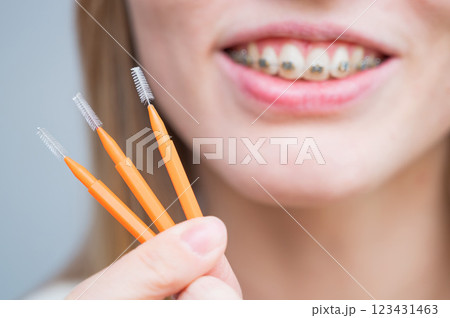 Close-up portrait of a woman with braces holding a floss to clean her teeth. Close-up portrait of a woman with braces holding a floss to clean her teeth. 123431463