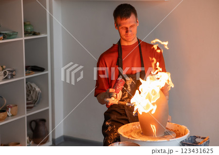 A potter burns a jug with a gas burner on a potter's wheel. A potter burns a jug with a gas burner on a potter's wheel. 123431625