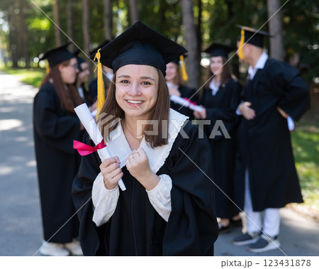 Group of happy students in graduation gowns outdoors. A young girl is happy to receive her diploma. 123431878