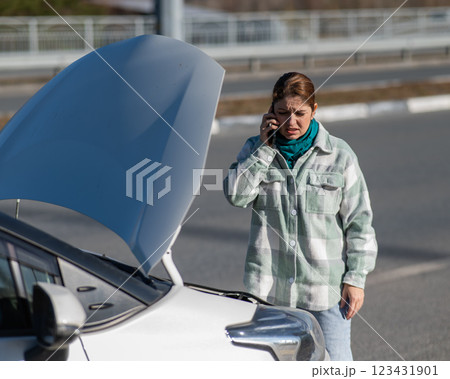 Caucasian woman cries and calls on the phone standing near the car with the hood open.  123431901