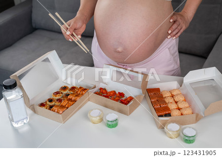 A pregnant woman holds chopsticks and stands at the table with rolls. Close-up of the belly. A pregnant woman holds chopsticks and stands at the table with rolls. Close-up of the belly. 123431905