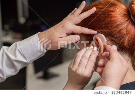 Man putting hearing aid on Caucasian red-haired woman. Man putting hearing aid on Caucasian red-haired woman. 123431947