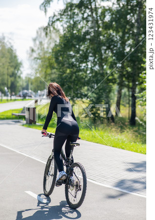 Rear view of Caucasian woman riding bike in park. Vertical photo.  123431974