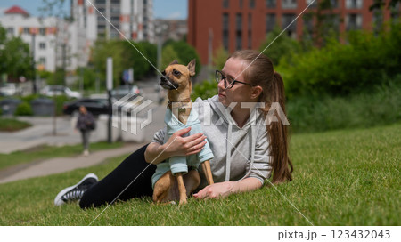 Young Caucasian woman lying on the lawn while walking with a small dog.  123432043