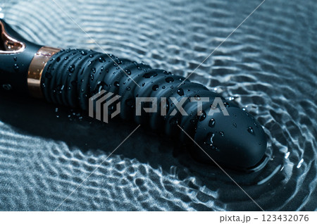 Black silicone vibrator in water. Circles on water around sex toy.  123432076