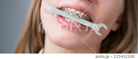 Close-up portrait of a woman with braces holding a wrench in her teeth. Close-up portrait of a woman with braces holding a wrench in her teeth. 123432100