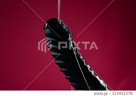 Lube pouring on black dildo on pink background.  123432276