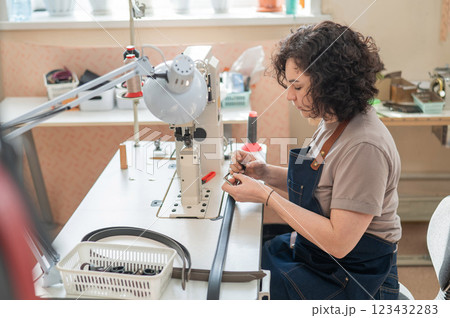 A woman tanner sews a leather belt on a sewing machine.  123432283
