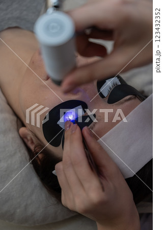 A woman undergoing eyelash extension procedure using an ultraviolet lamp. A woman undergoing eyelash extension procedure using an ultraviolet lamp. 123432352