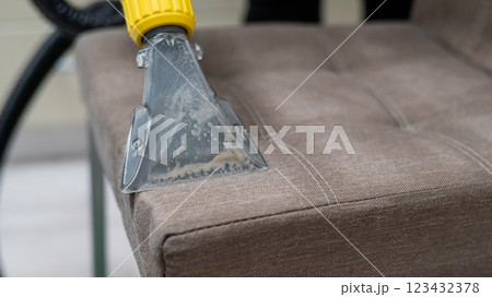 Woman cleaning a fabric chair with a professional washing vacuum cleaner.  123432378