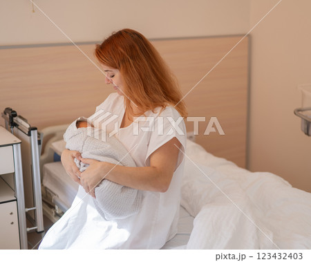 Caucasian woman holding newborn son while sitting on couch in maternity hospital ward. Caucasian woman holding newborn son while sitting on couch in maternity hospital ward. 123432403