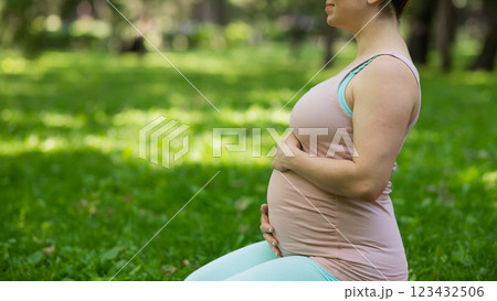 Pregnant caucasian woman doing yoga in the park. Close-up of the abdomen. 123432506
