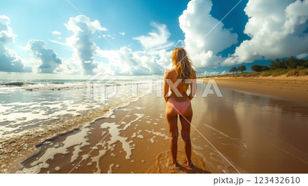 A woman in a bikini standing on a beach looking out at the ocean A woman in a bikini standing on a beach looking out at the ocean 123432610